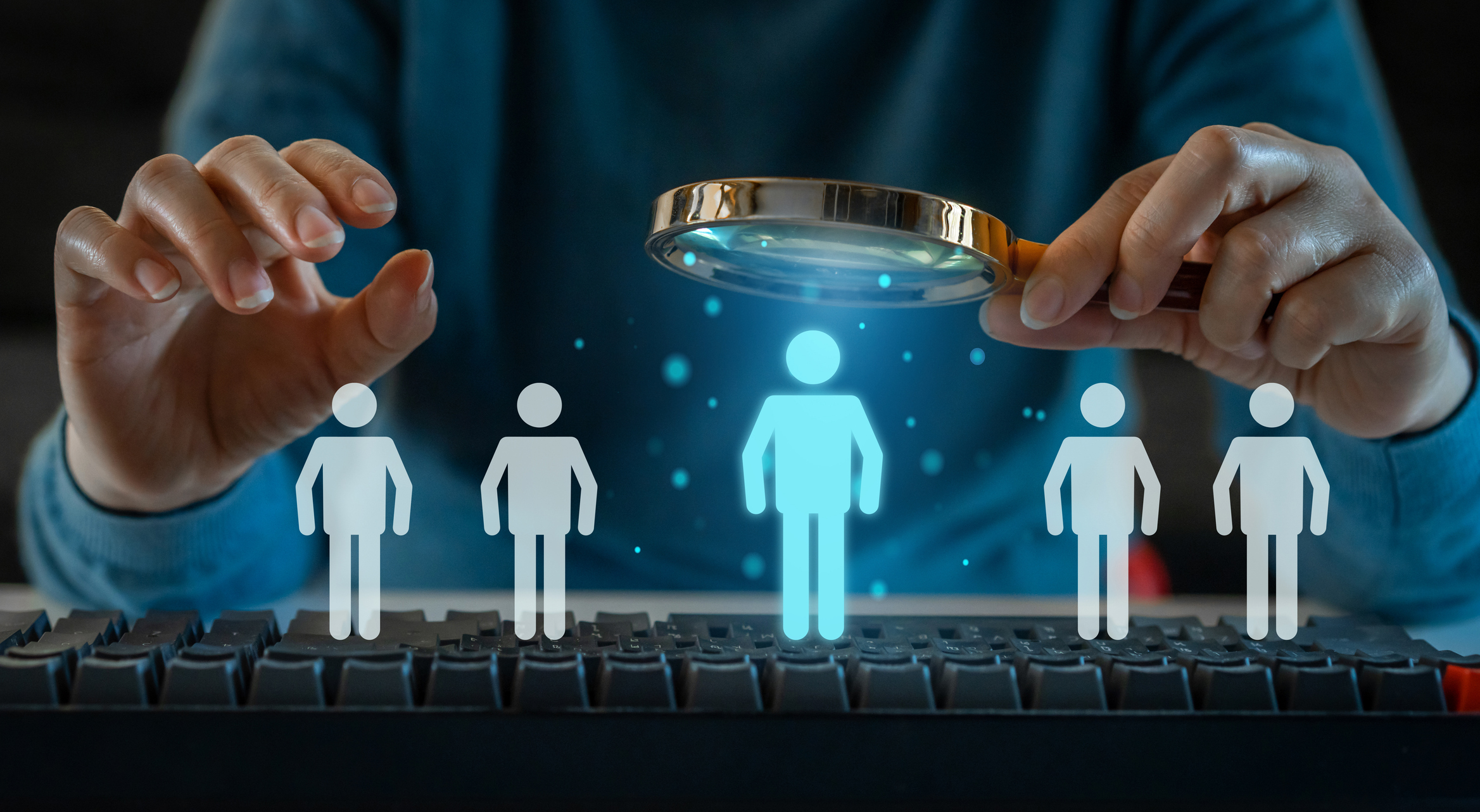 A hand highlights a glowing figure among others above a keyboard.