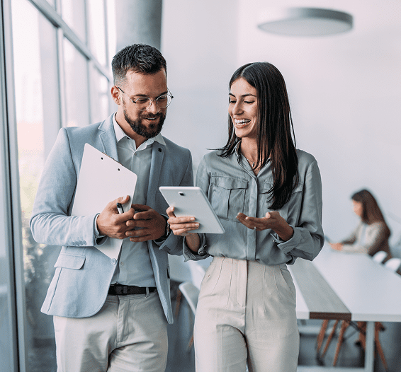 Two professionals smiling and discussing work on a tablet in a modern office.