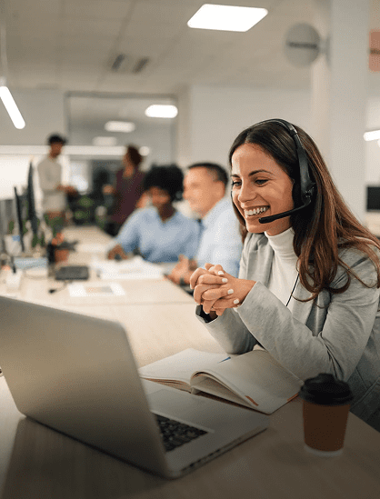 A woman happily working at a call center with a headset and laptop.