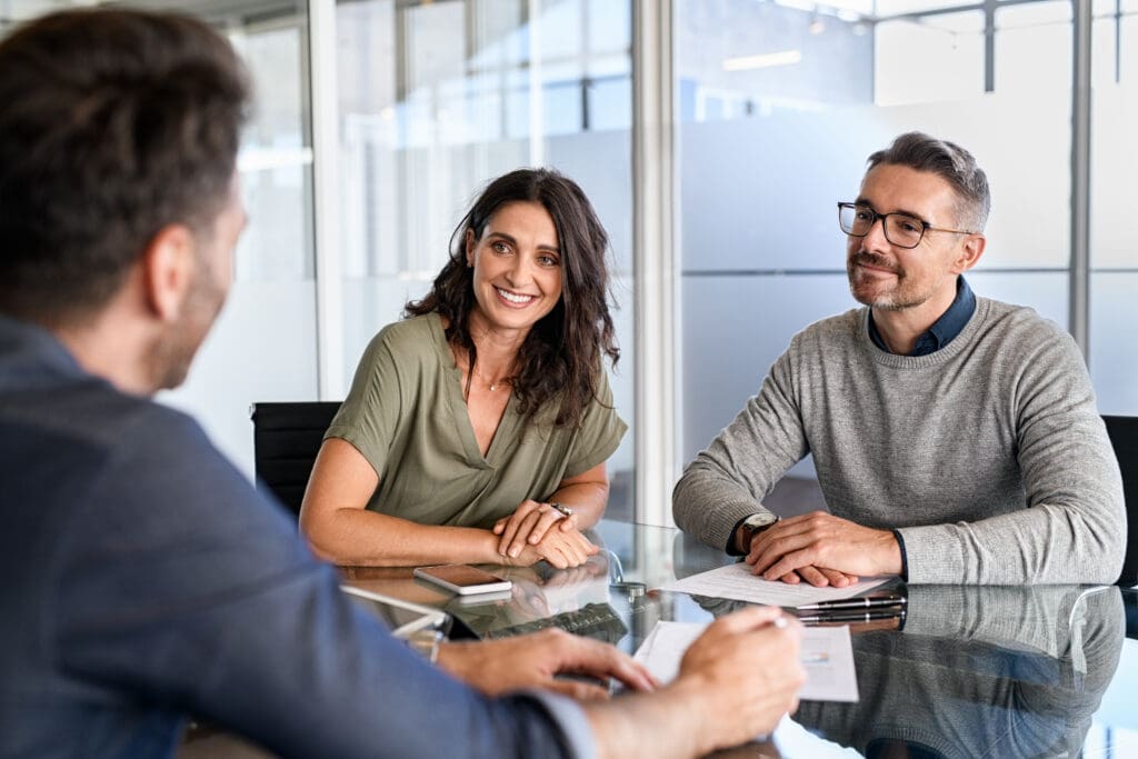 Three professionals engaged in a friendly meeting around a glass table.