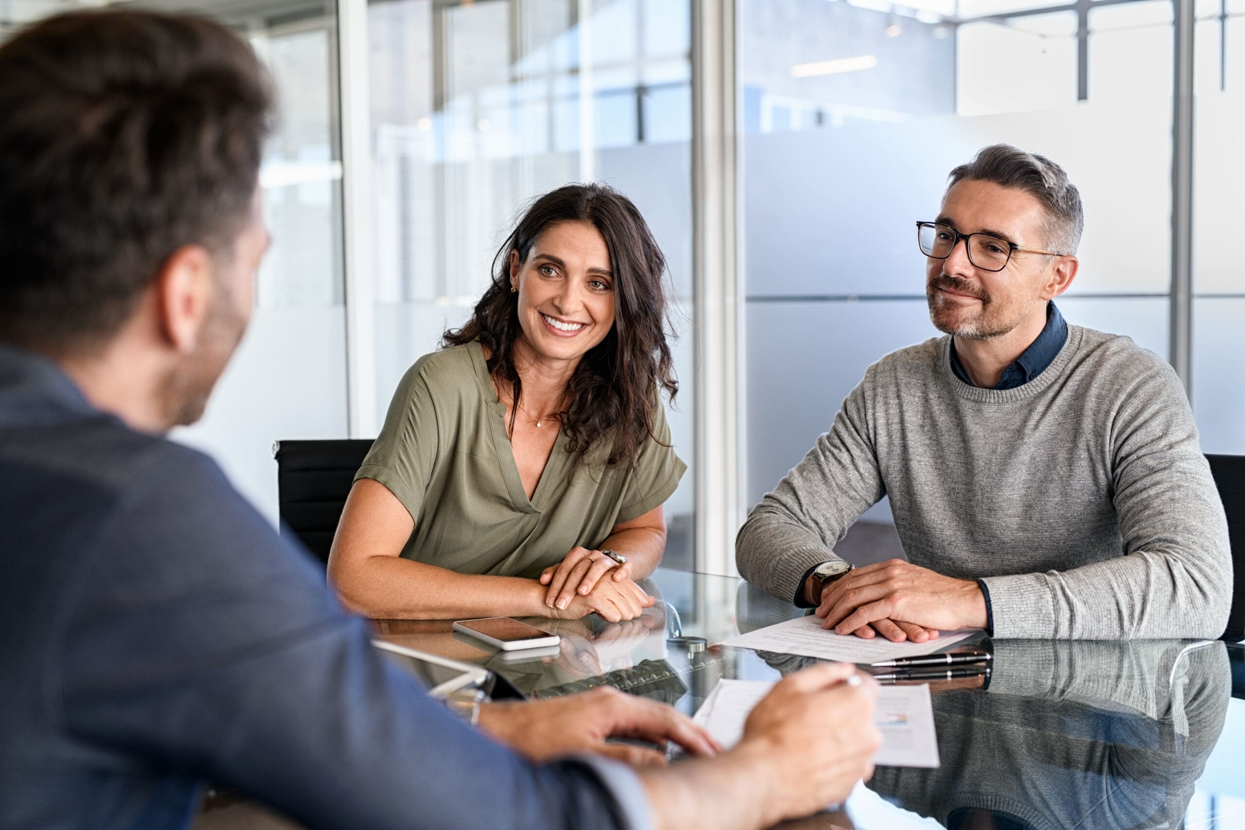 Three professionals engaged in a friendly meeting around a glass table.
