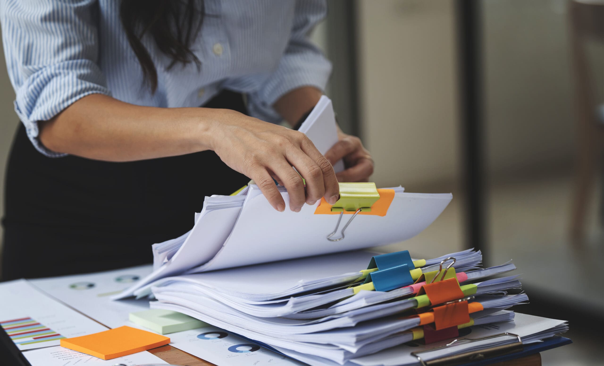 Person organizing documents with colorful tabs on a desk.