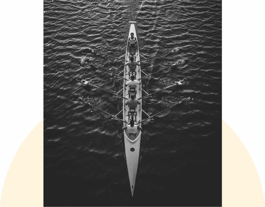 A rowing team in a long boat on dark water, viewed from above.