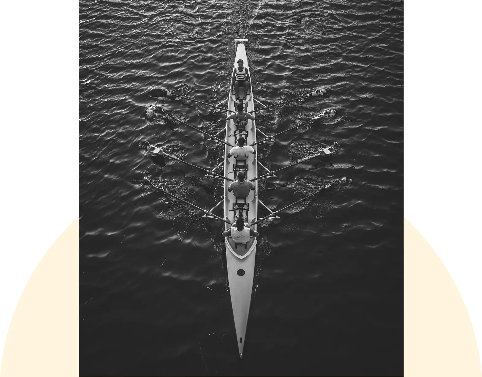 A rowing team in a long boat on dark water, viewed from above.